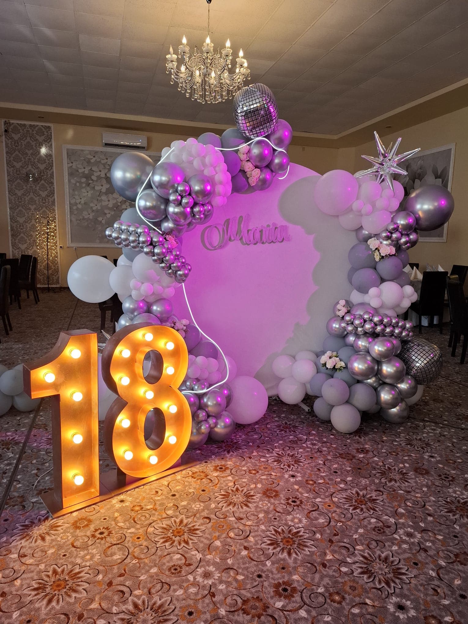 Colț foto de majorat cu lumini roz, baloane argintii și cifra 18